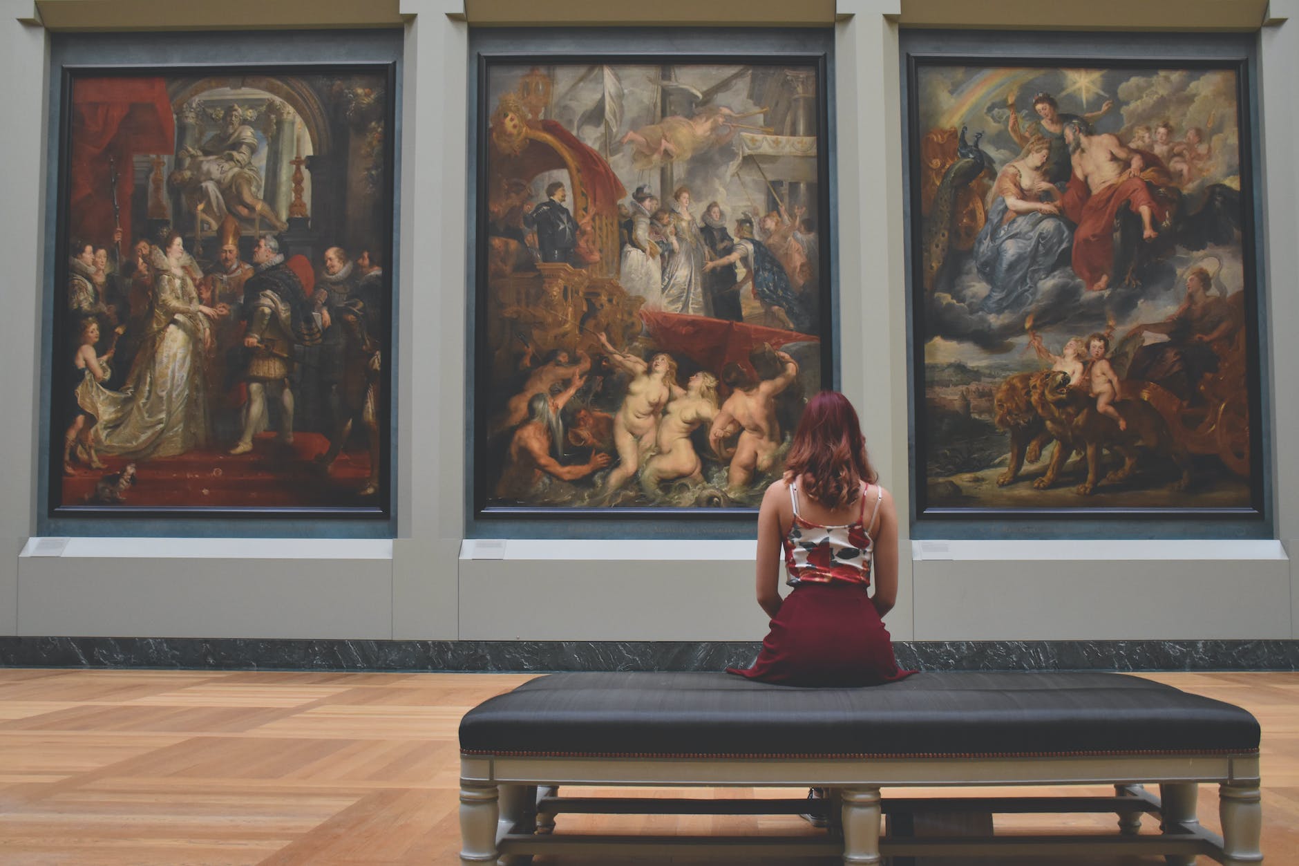 woman sitting on ottoman in front of three paintings